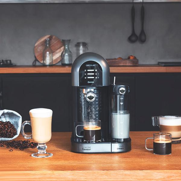 Una macchina da caffè nera e argentata con due bicchieri di caffè e un contenitore per il latte su un bancone.