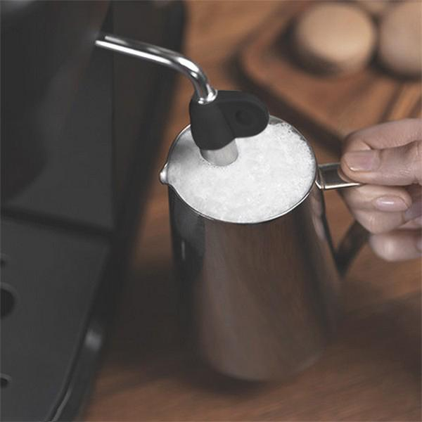 Die Hand einer Person schäumt Milch mit einer Maschine auf. Die Milch befindet sich in einem Metallkrug, die Maschine ist schwarz.