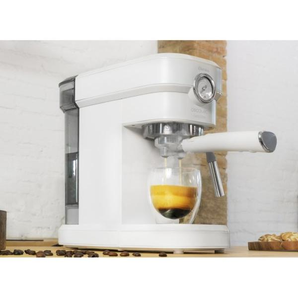 Macchina per espresso bianca con una tazza di vetro sotto. Il caffè si versa nella tazza, chicchi vicini.