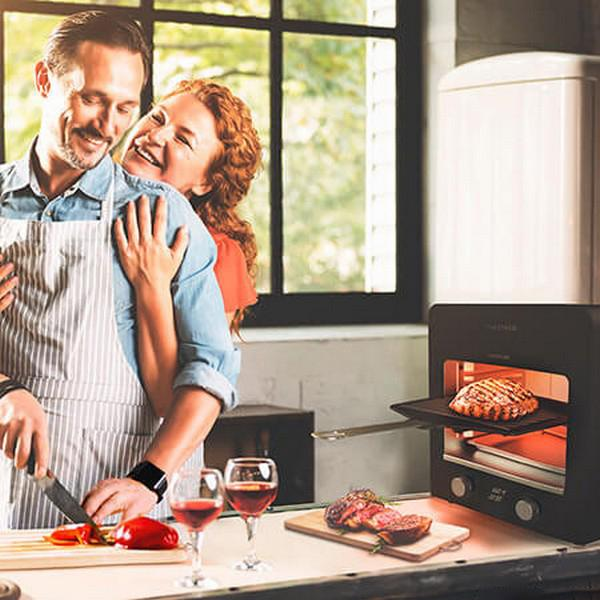 Koppel in de keuken. Vrouw omhelst man, die snijdt. Biefstuk in oven en op houten plank.