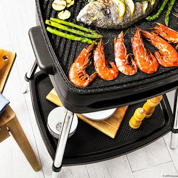 Una parrilla con comida incluyendo pescado, camarones y verduras, sobre bandeja y tabla de madera.