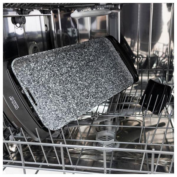 Wnętrze zmywarki z szarą patelnią grillową i czarnym stojakiem. Widoczne inne części.
