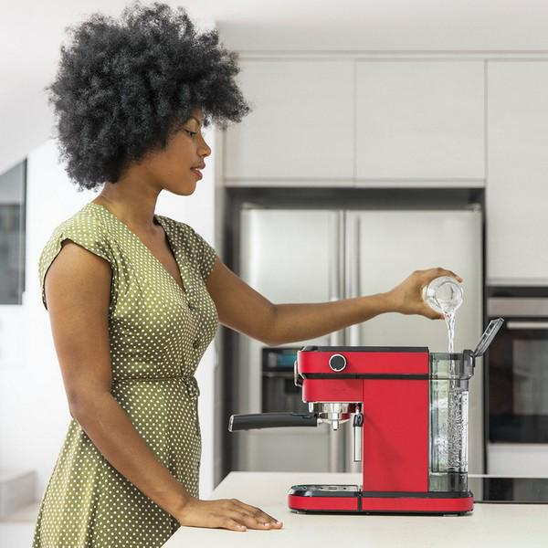 Frau gießt Wasser in eine rote Kaffeemaschine, in einer modernen Küche stehend.