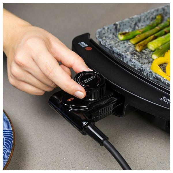 Ręka reguluje czarne pokrętło na grillu. Szparagi i papryka są grillowane.