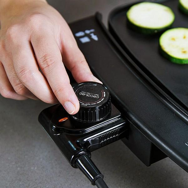 Persona regola manopola nera su elettrodomestico nero. Zucchine affettate accanto.