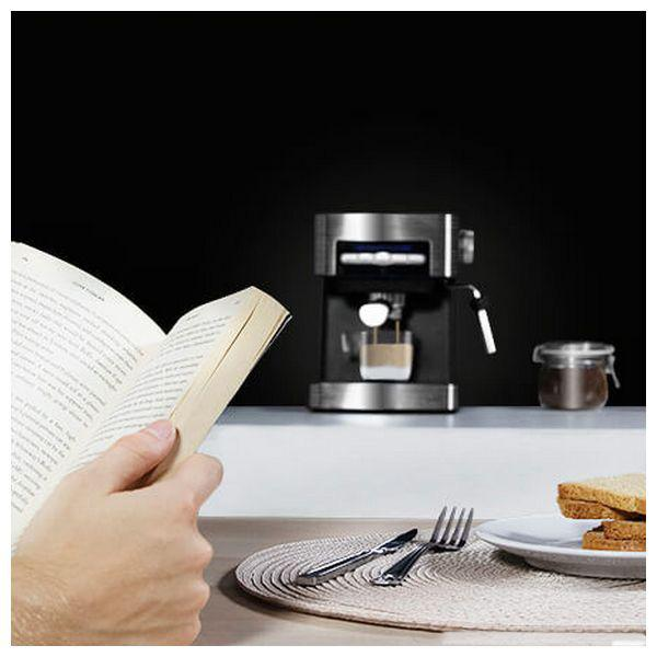 Persona che legge un libro con macchina del caffè e cibo sullo sfondo. Tavola apparecchiata.