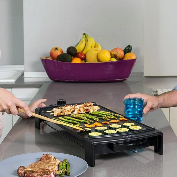 Griglia con verdure e spiedini. Persone con piatto e bicchiere d'acqua. Frutta sullo sfondo.