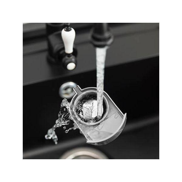 Woda płynie z kranu do szarego filtra. Filtr znajduje się w czarnym zlewie.