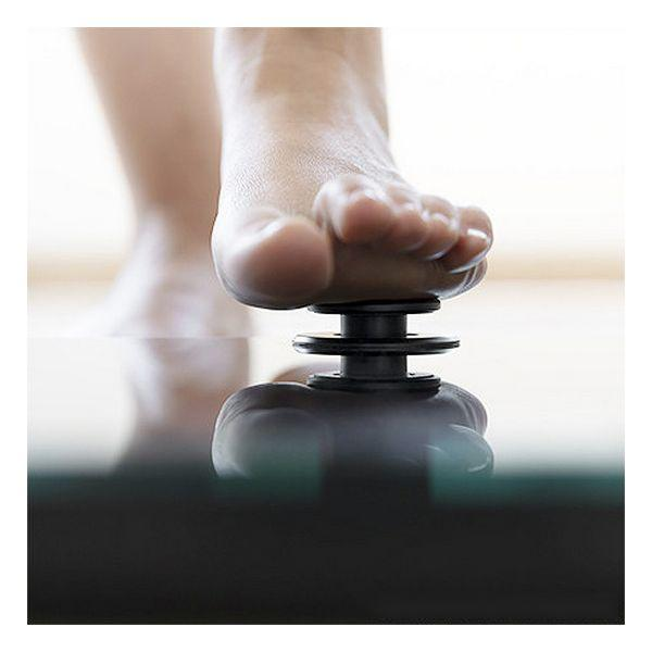 Stopa stąpająca na czarnym, sprężynowym urządzeniu, odbijająca się na szklanej powierzchni. Jasne tło.