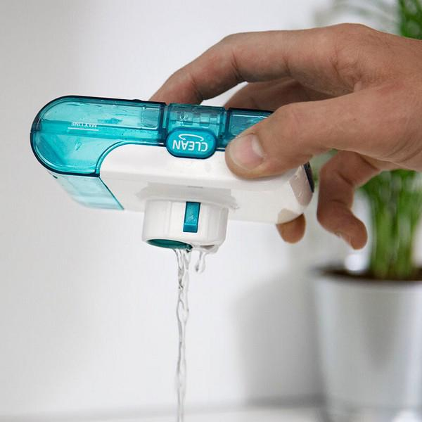 Eine Hand, die einen türkis-weißen Wasserfilter hält, aus dem Wasser fließt, in der Nähe einer Pflanze.