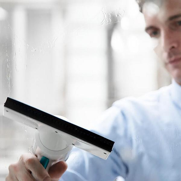 Ein Mann putzt mit einem Abzieher ein Fenster. Er trägt ein blaues Hemd. Das Glas ist nass.
