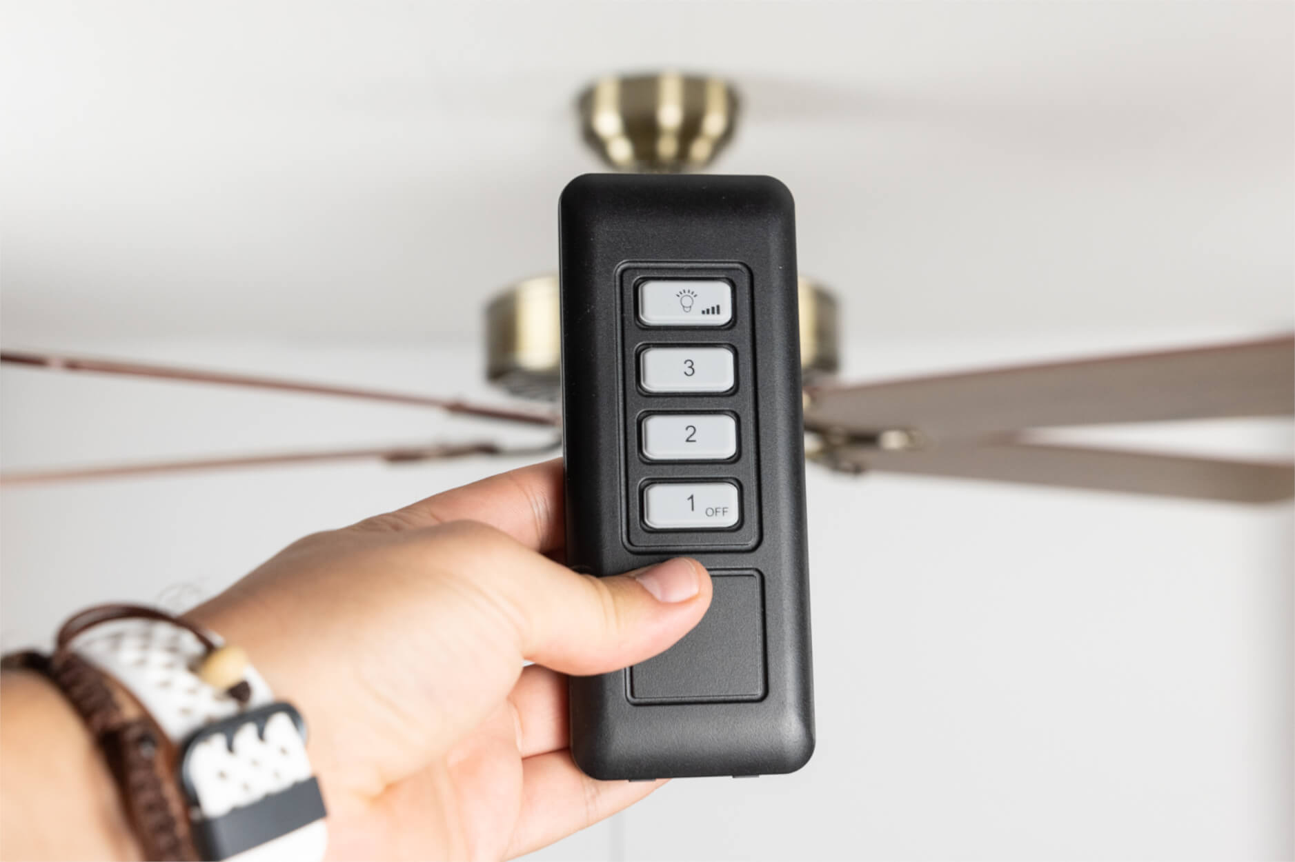 Eine Hand hält eine schwarze Fernbedienung mit Tasten zur Steuerung eines Deckenventilators.