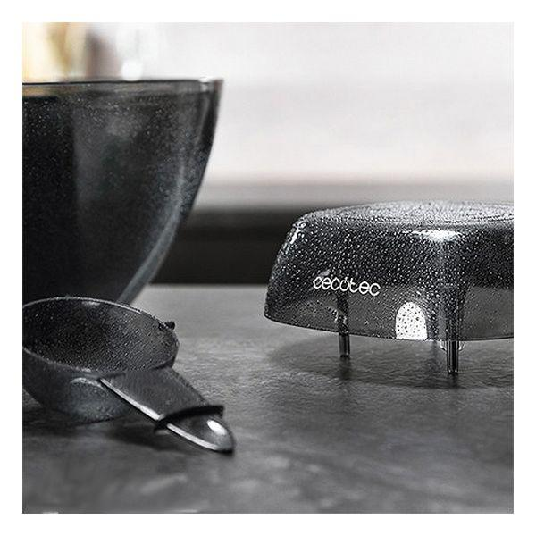 Parti nere di un robot da cucina su una superficie grigia. Include una ciotola, un cucchiaio e un coperchio.