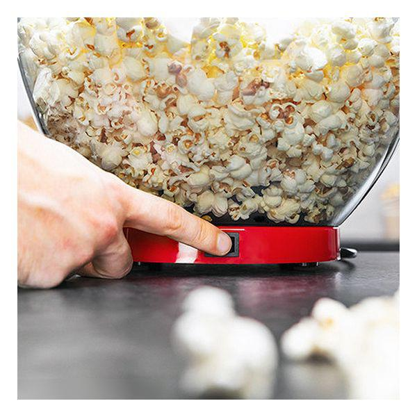 Una mano preme un pulsante su una macchina per popcorn rossa, piena di popcorn.