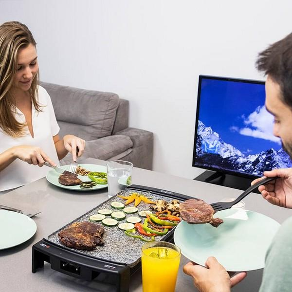 Para grilluje jedzenie na stole z grillem. Warzywa i mięso na talerzu, TV w tle.