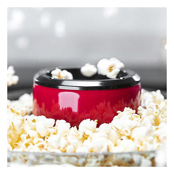Una macchina per popcorn rossa piena di popcorn, circondata da popcorn su una superficie riflettente.