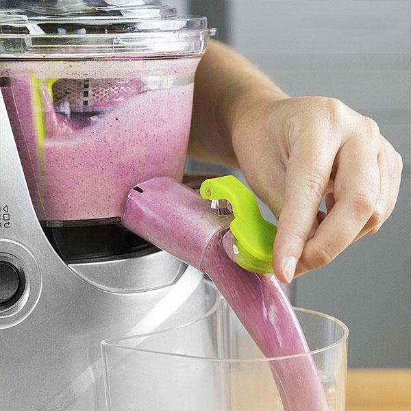 Una mano está usando una licuadora para extraer jugo, con una sustancia morada que fluye a un recipiente.