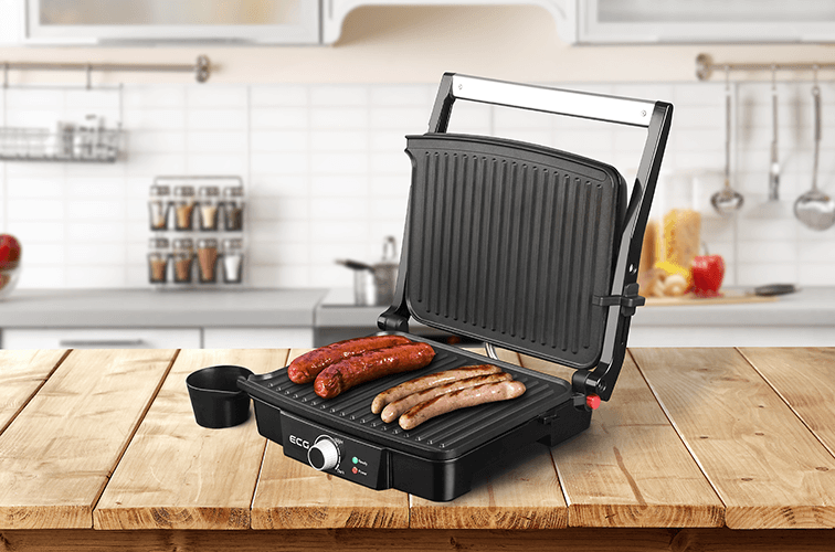 Parrilla eléctrica con salchichas a la parrilla. El fondo incluye una cocina con encimera de madera y armarios.