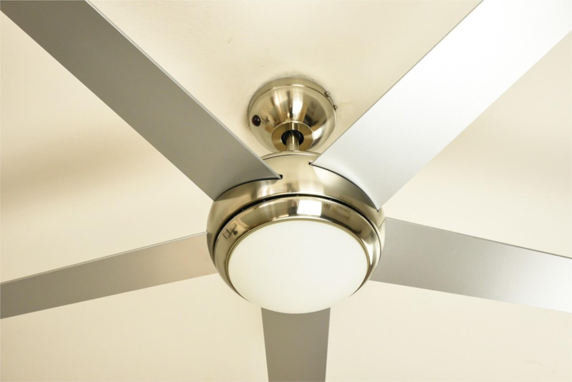Ein Deckenventilator mit fünf silbernen Flügeln, einer zentralen Leuchte und einer weißen Decke.