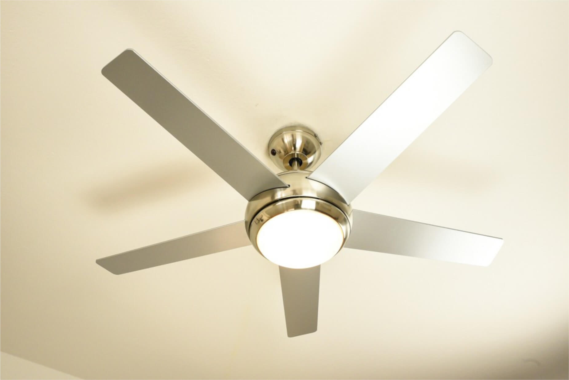 Ein Deckenventilator mit fünf Flügeln und einer Lichtvorrichtung, montiert an einer beige Decke.