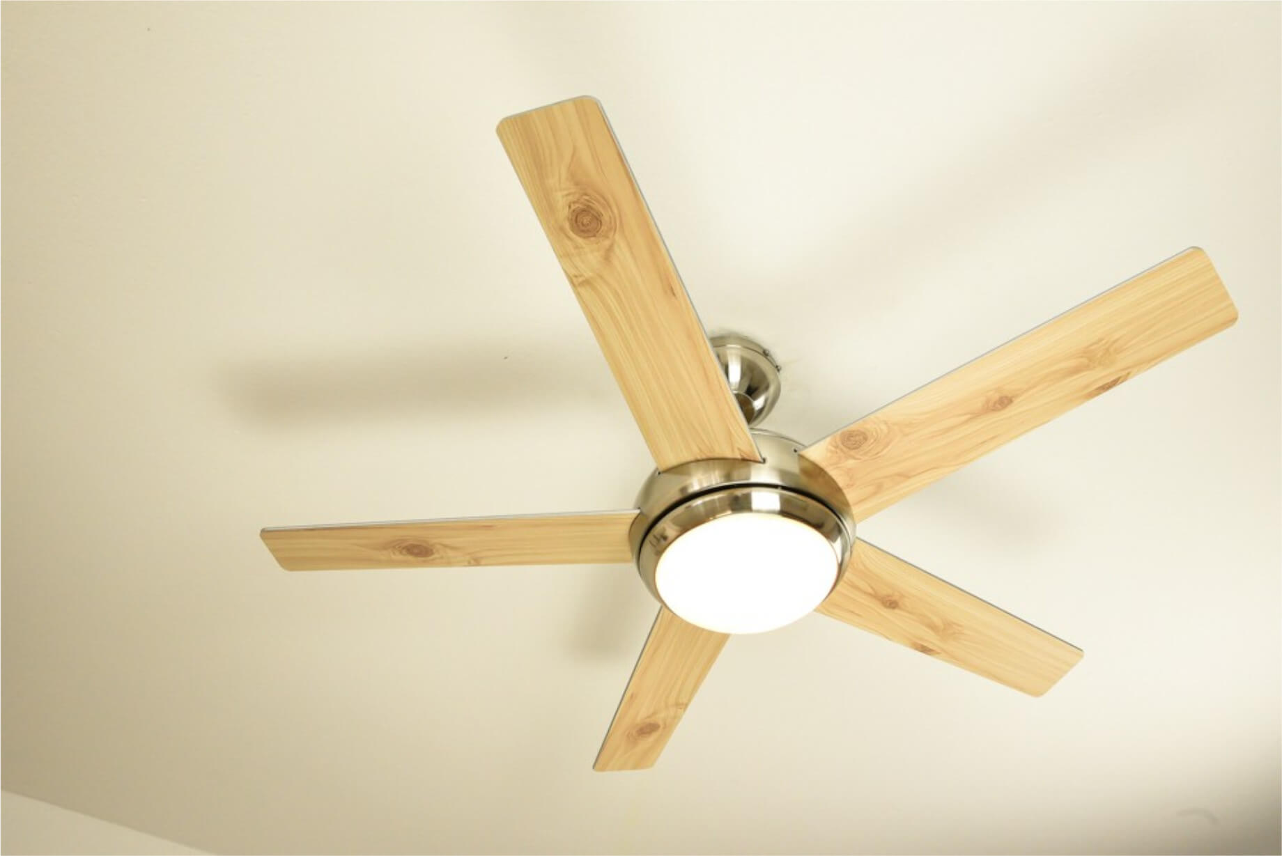 Deckenventilator mit fünf hellen Holzblättern und einem Mittellicht.