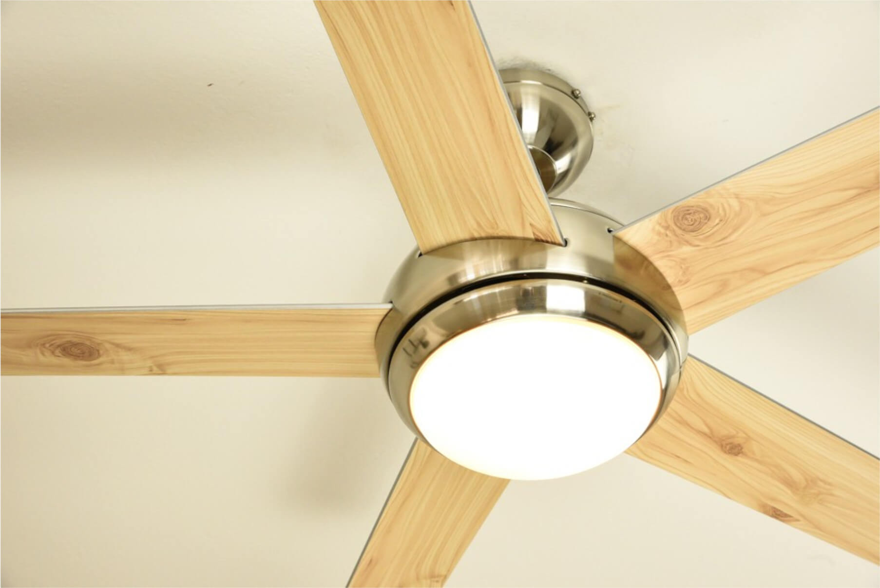 Deckenventilator mit Holzblättern und zentralem Licht. Der Ventilator ist an einer weißen Decke montiert.
