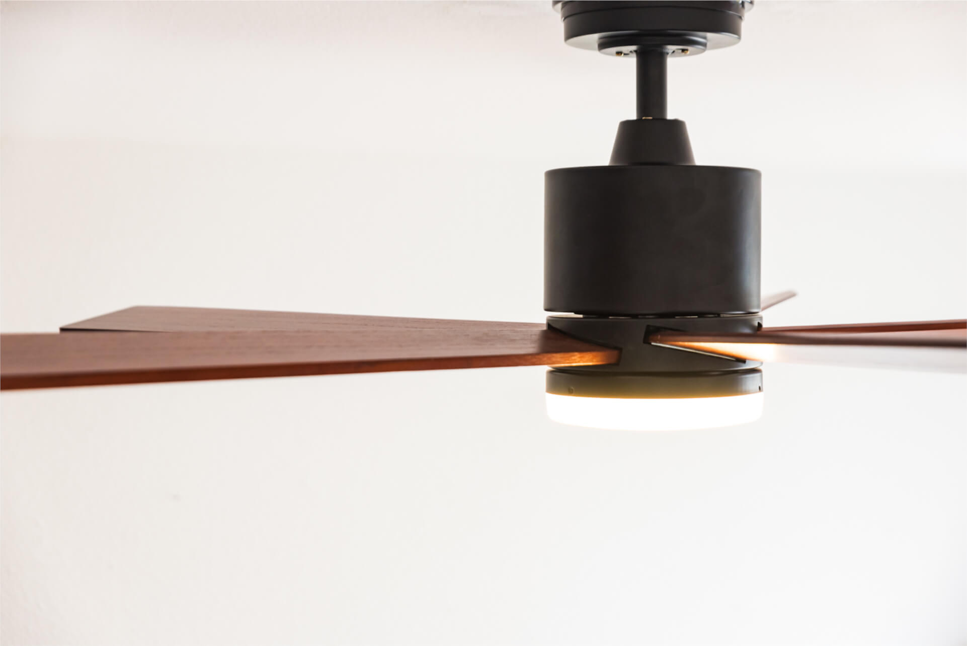 Ein Deckenventilator mit Holzflügeln und Licht. Der Hintergrund ist weiß. Der Ventilator ist aus.