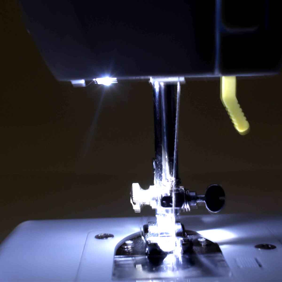 Zbliżenie igły maszyny do szycia i światła, oświetlającego obszar roboczy.