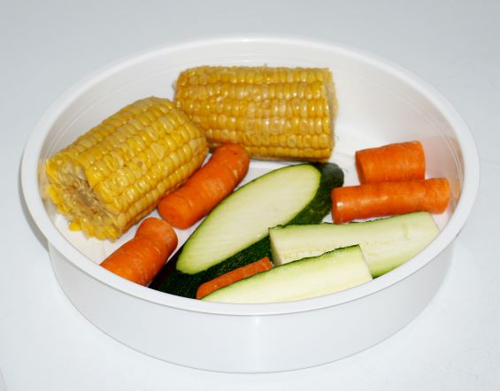 Weiße Schüssel mit Mais, Karotten und Zucchinischeiben.