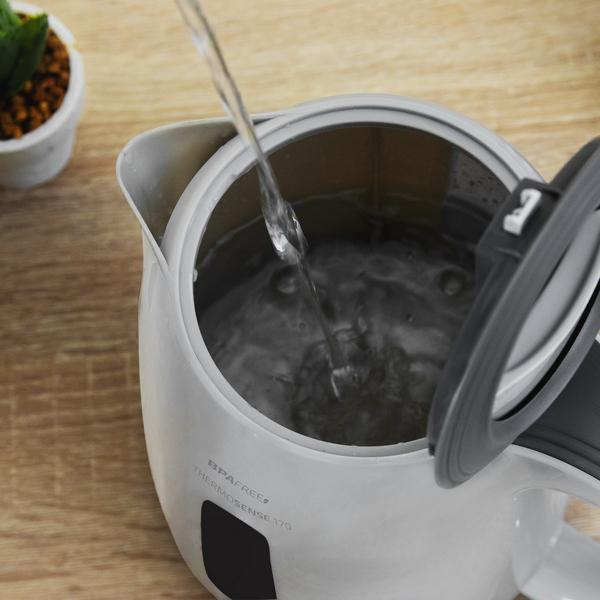 Acqua versata in un bollitore elettrico bianco e aperto su una superficie di legno.