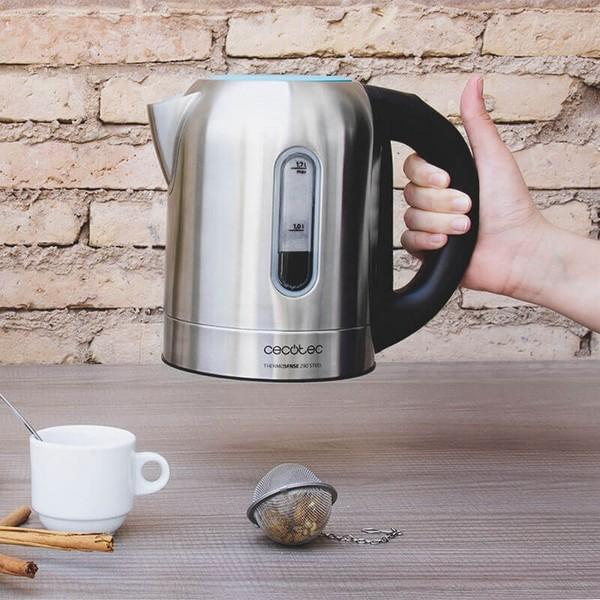 Roestvrijstalen elektrische waterkoker die door een hand wordt vastgehouden, met een kopje en thee-infuser ernaast.