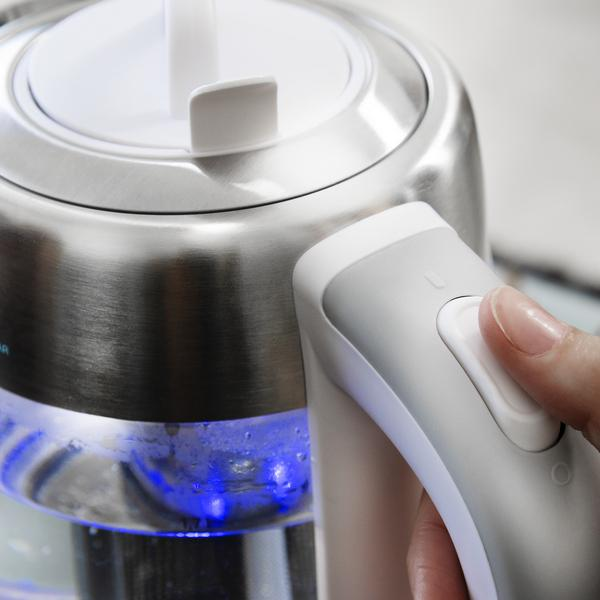 Eine Hand drückt einen Knopf an einem silber-weißen elektrischen Wasserkocher.