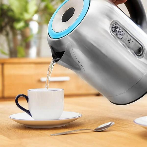 Waterkoker giet water in een witte kop op een schotel, met een lepel op een houten tafel.