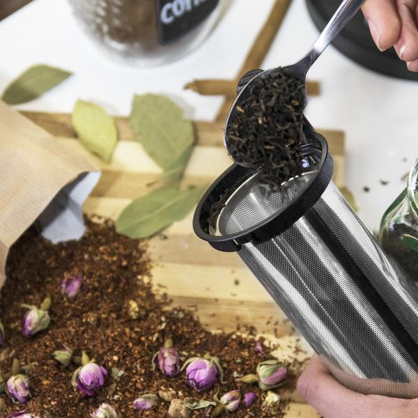 Una persona vertiendo hojas de té sueltas en un infusor de té con una cuchara.