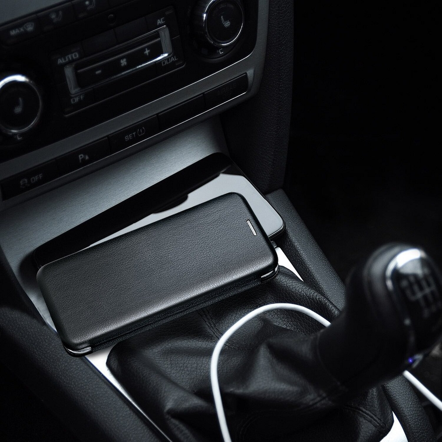 Schwarze Handyhülle auf schwarzem Handy in Autokonsole, weißes Kabel.