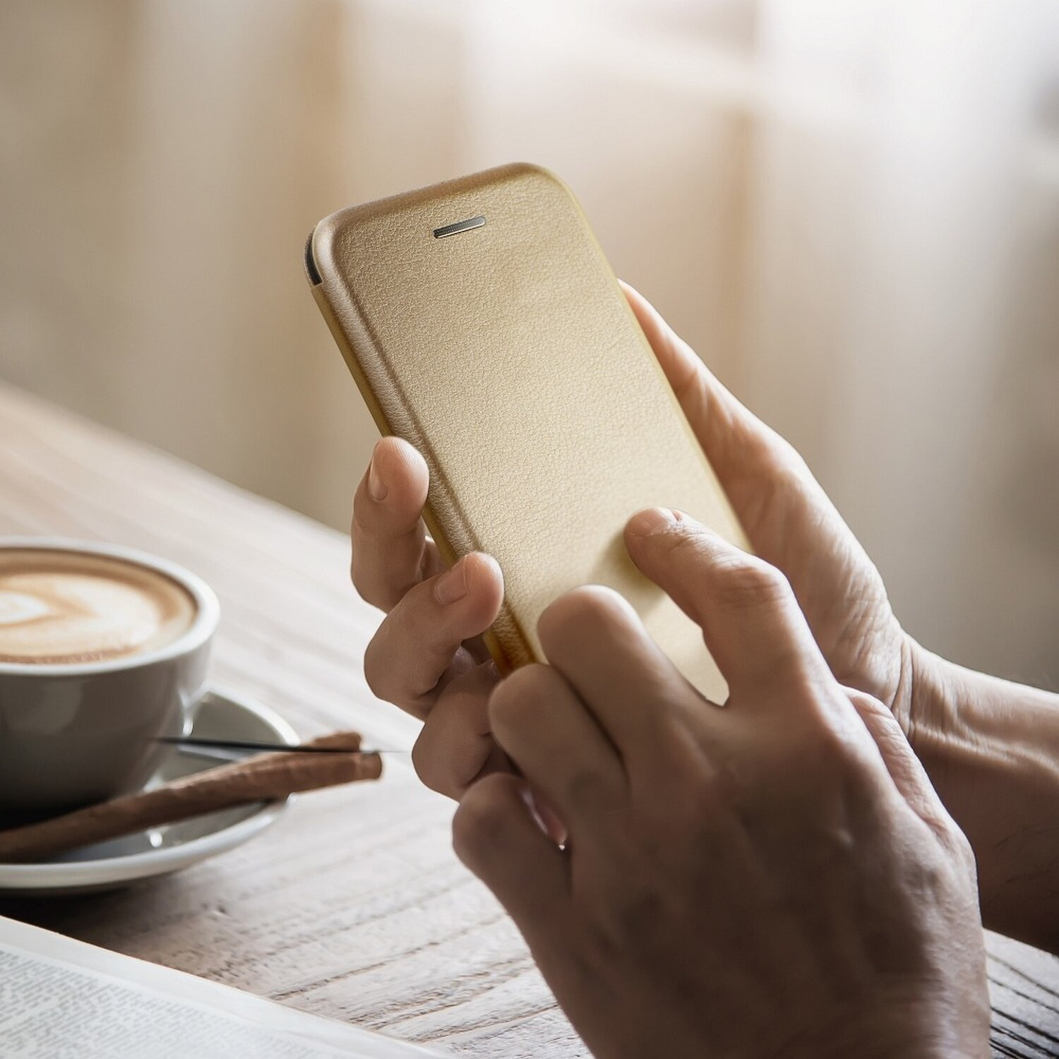 Eine Person hält ein goldenes Telefon, neben Kaffee und Zimtstangen auf einem Tisch.