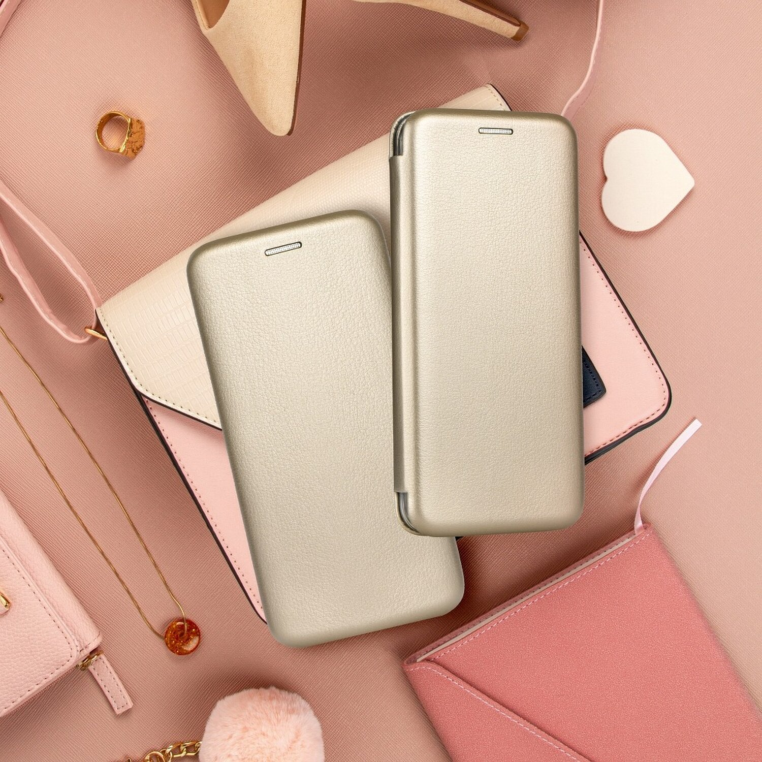 Zwei goldene Handyhüllen auf rosa Hintergrund mit Accessoires: Geldbörse, Ring, Halskette und Herzform.