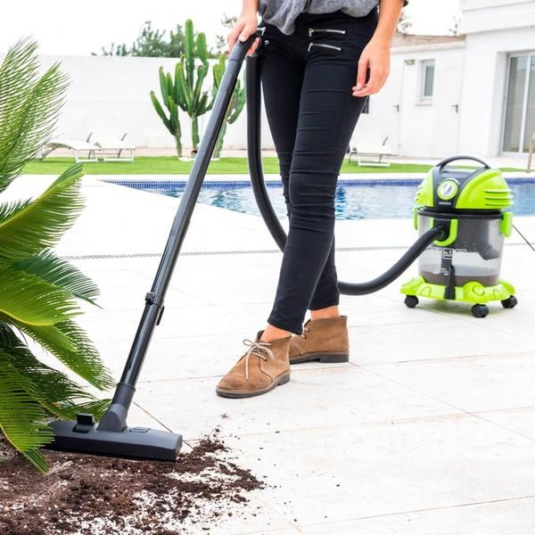 A woman vacuuming outside, dirt on the ground and a green vacuum cleaner.