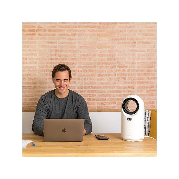 Mężczyzna siedzi przy biurku z laptopem, uśmiecha się, i biały oczyszczacz powietrza.