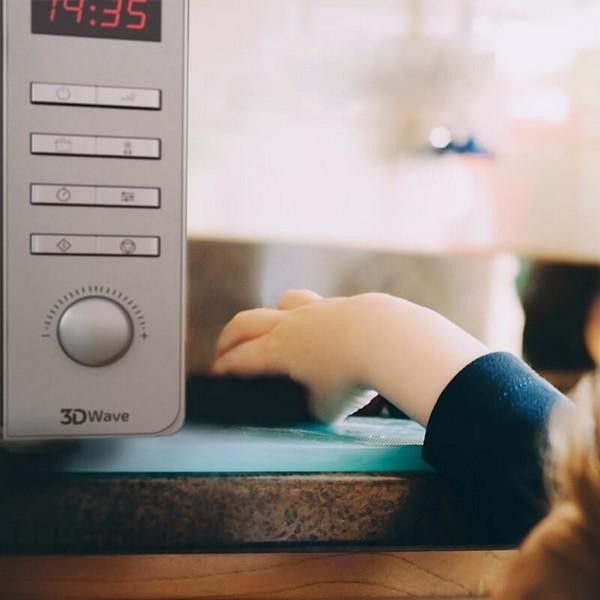 Ręka dziecka w pobliżu panelu sterowania kuchenki mikrofalowej, wyświetlającego godzinę 14:35.