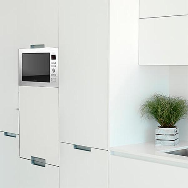 Wbudowana kuchenka mikrofalowa w białych szafkach kuchennych, z rośliną na blacie.