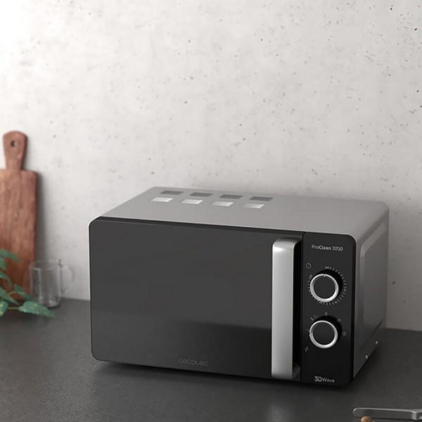 Czarna kuchenka mikrofalowa ze srebrnym blatem. Umieszczona na blacie kuchennym z drewnianą deską do krojenia.