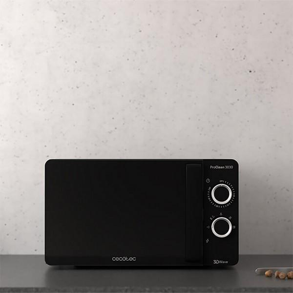 Czarna kuchenka mikrofalowa na stole, jasnoszara ściana w tle.