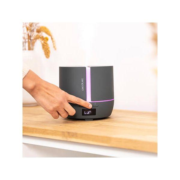 Czarny i szary dyfuzor na drewnianym stole. Dłoń naciska przycisk. Tło jest rozmyte.