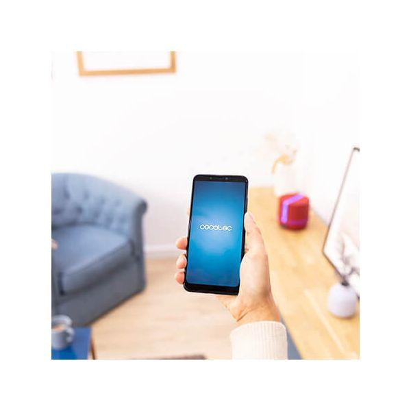 Osoba trzymająca czarny smartfon z niebieskim ekranem, w pomieszczeniu. Czerwony głośnik w tle.