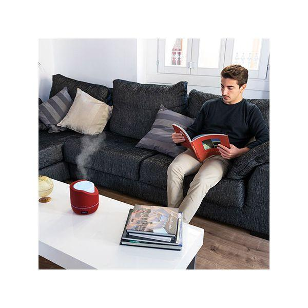 Mężczyzna czyta książkę na kanapie. Czerwony dyfuzor i książki na stole.