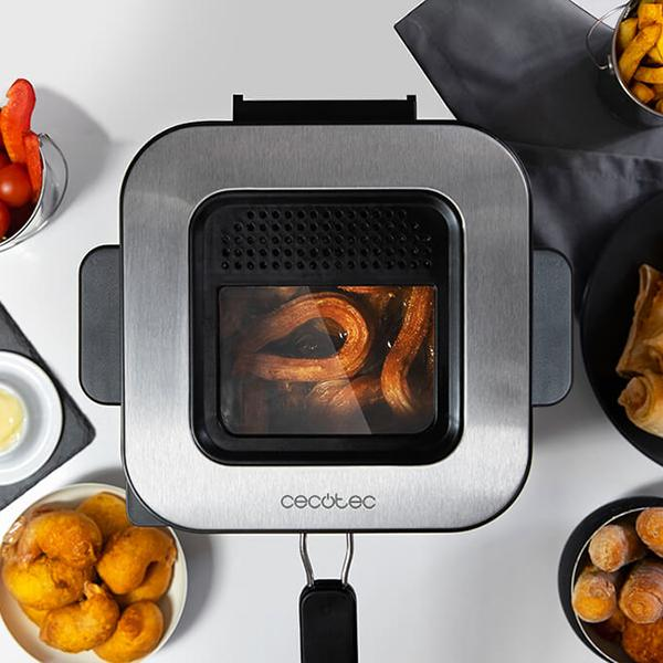 Frytkownica beztłuszczowa ze stali nierdzewnej z jedzeniem w środku i miskami z jedzeniem. Białe tło.