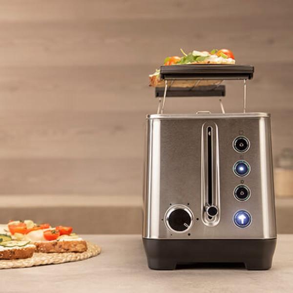 Silberner Toaster mit Toast darauf. Zwei Toastscheiben auf einem Teller im Vordergrund.