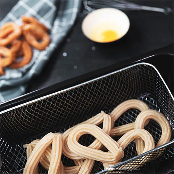 Churros w metalowym koszu na czarnej powierzchni. Obok miska z jajecznicą i ściereczka kuchenna.