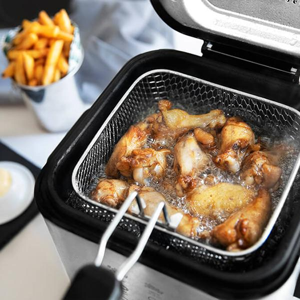 Frytownica z kurczakiem w koszu, smażąca się w oleju. Wiadro frytek w tle.